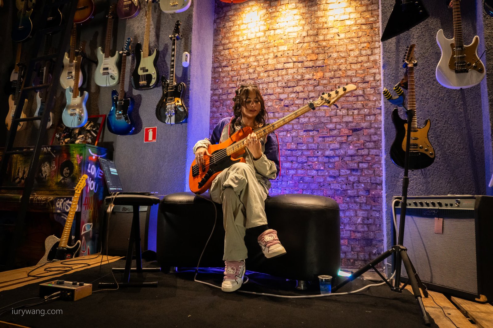 Palco da oficina na Aslan com a baixista sentada ao fundo e guitarras na parede