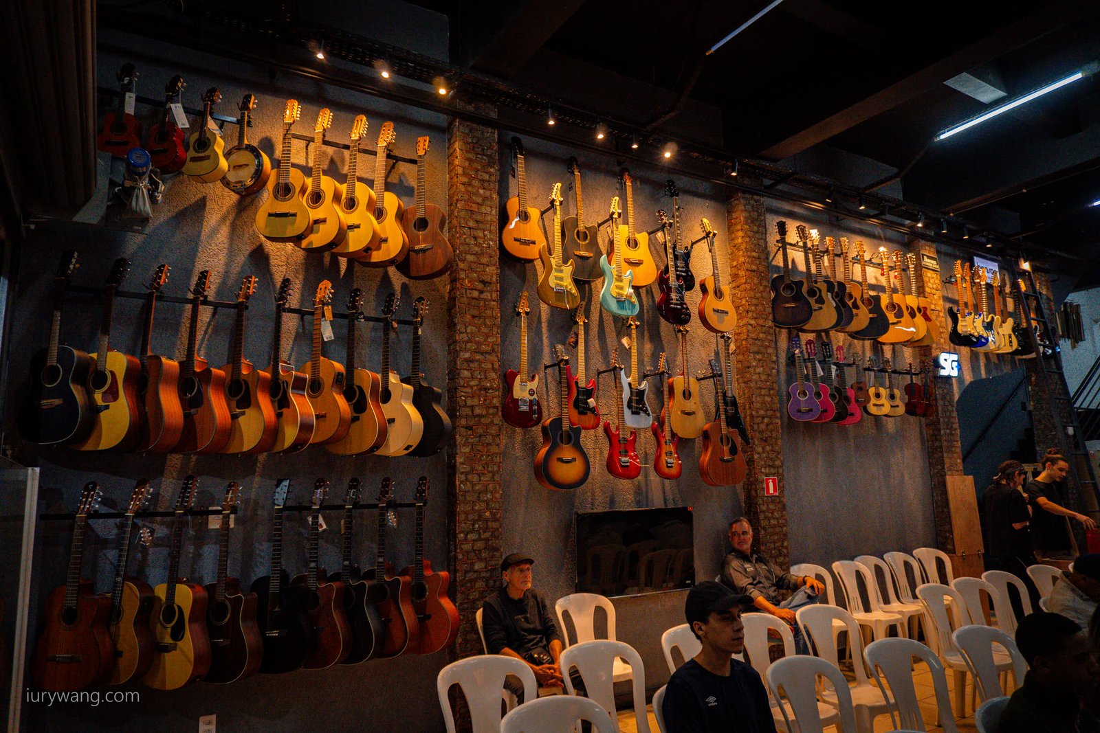 Parede de violões e guitarras da Aslan com a plateia sentada em cadeiras brancas