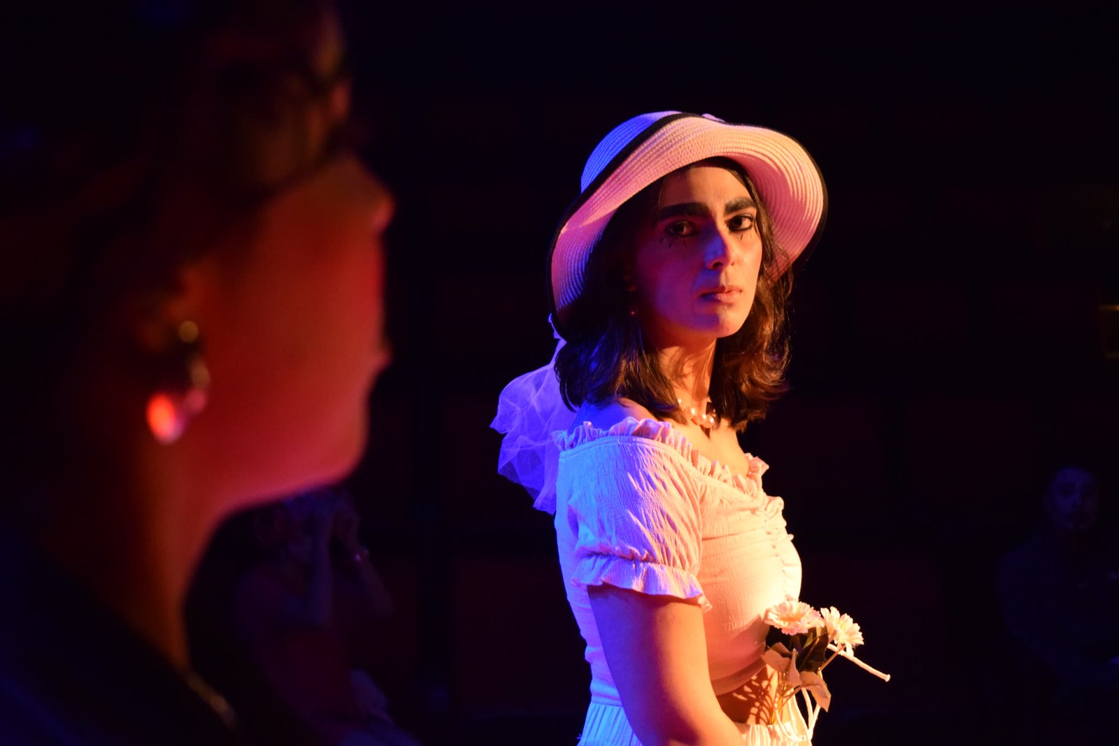 Atriz de chapéu e vestido branco com buquê em cena